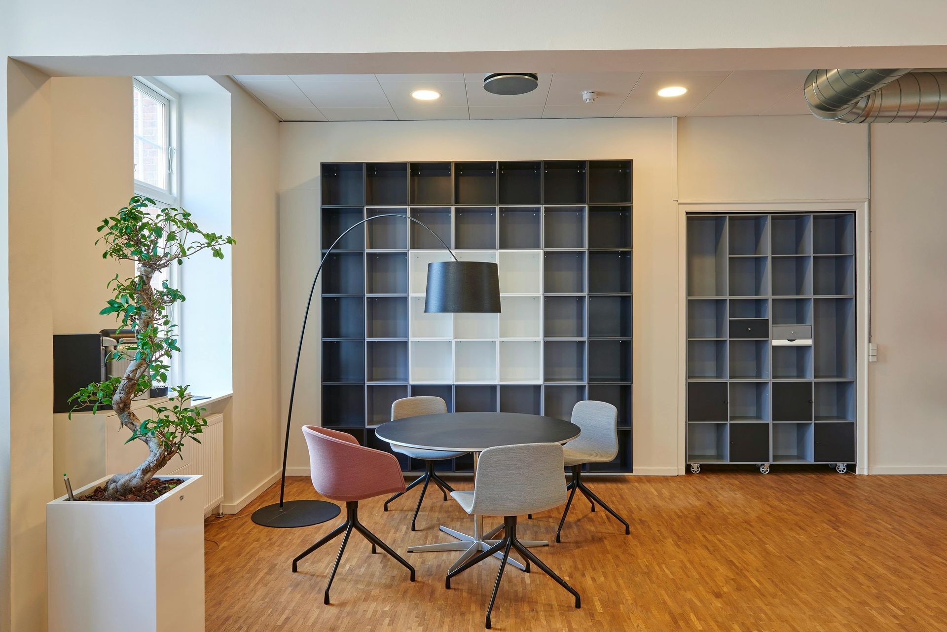 Modern office interior with a round table and chairs in front of a square shelving unit.